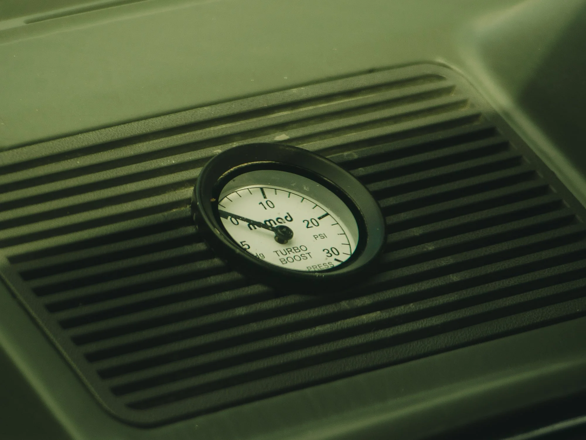 Close-up of a turbo boost pressure gauge on a car's dashboard, showing pressure in PSI with a red indicator needle.