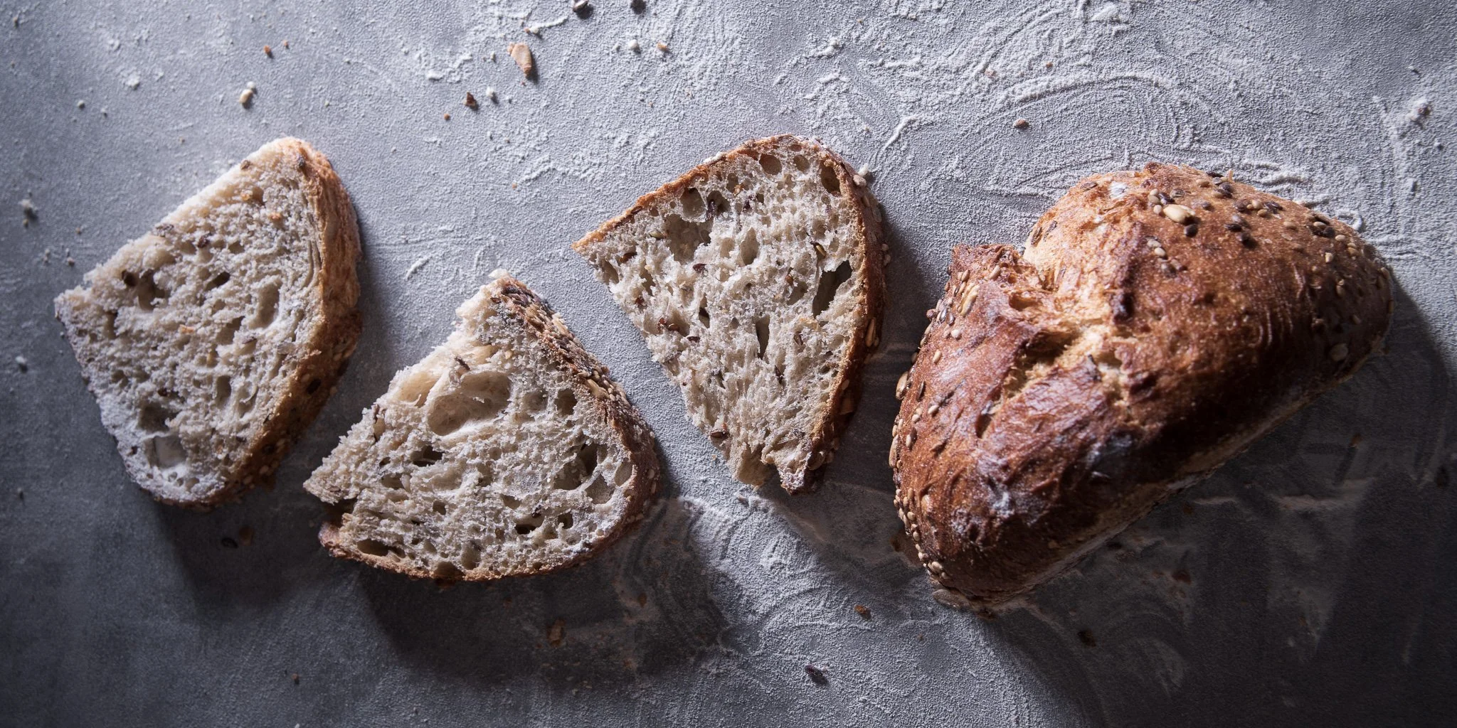 Sliced and whole multigrain bread on a textured gray surface.