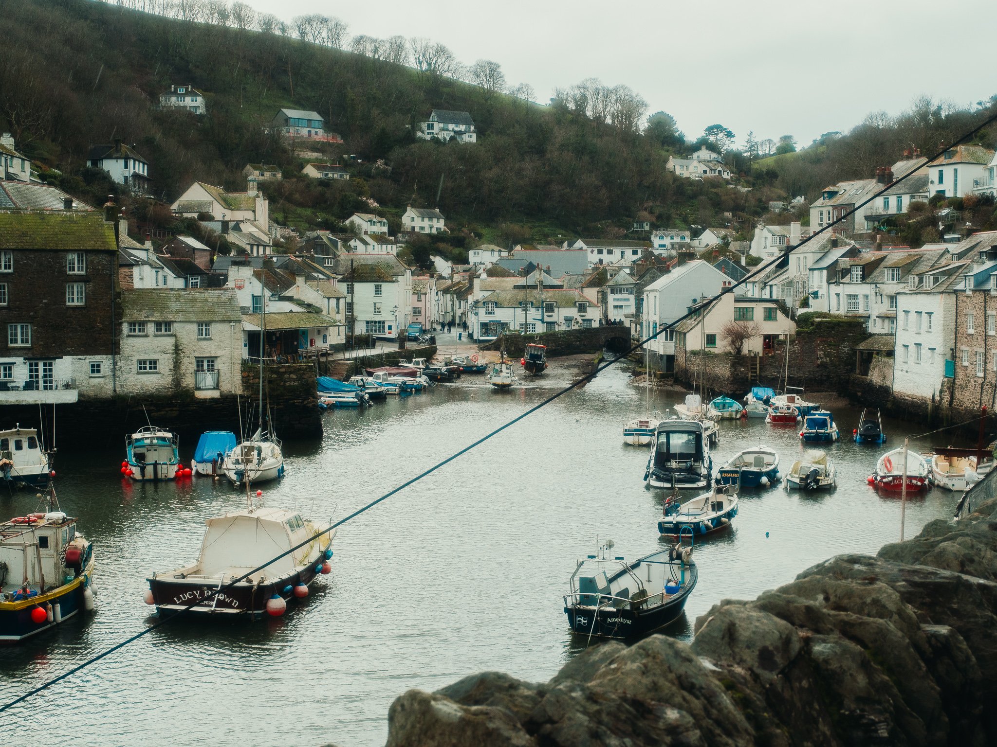 A harbor with boats docked along the water, surrounded by white buildings and houses up on green hills under a cloudy sky.