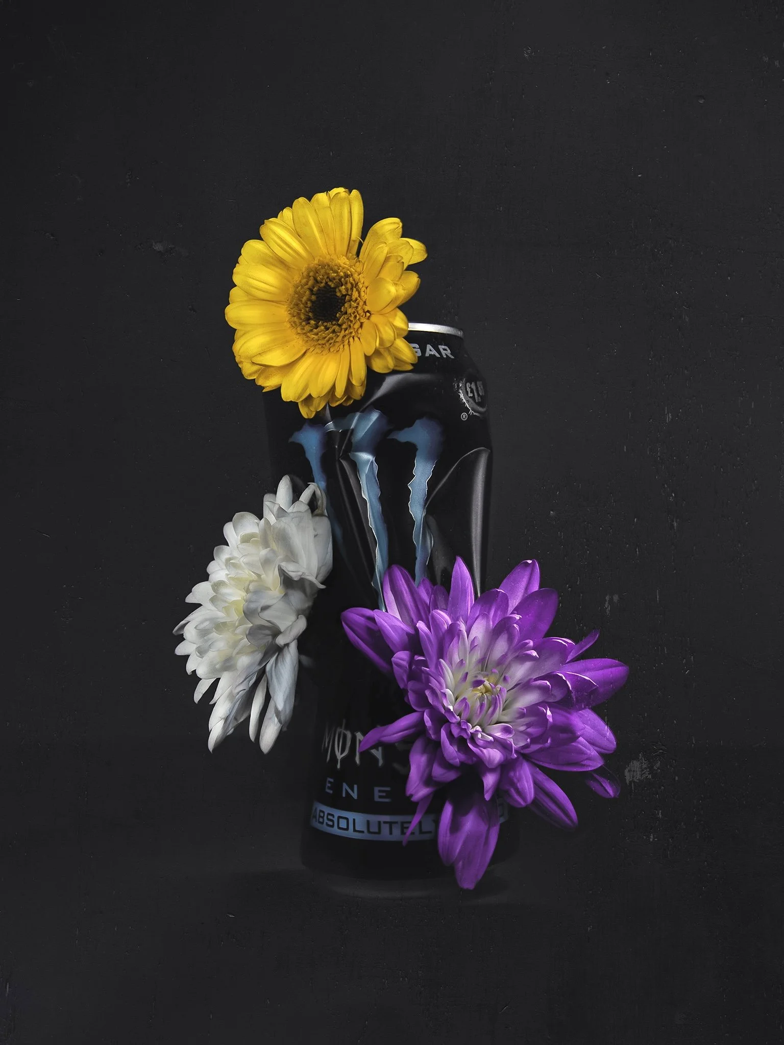 Black can of Monster energy drink adorned with yellow, white, and purple flowers on a black background.