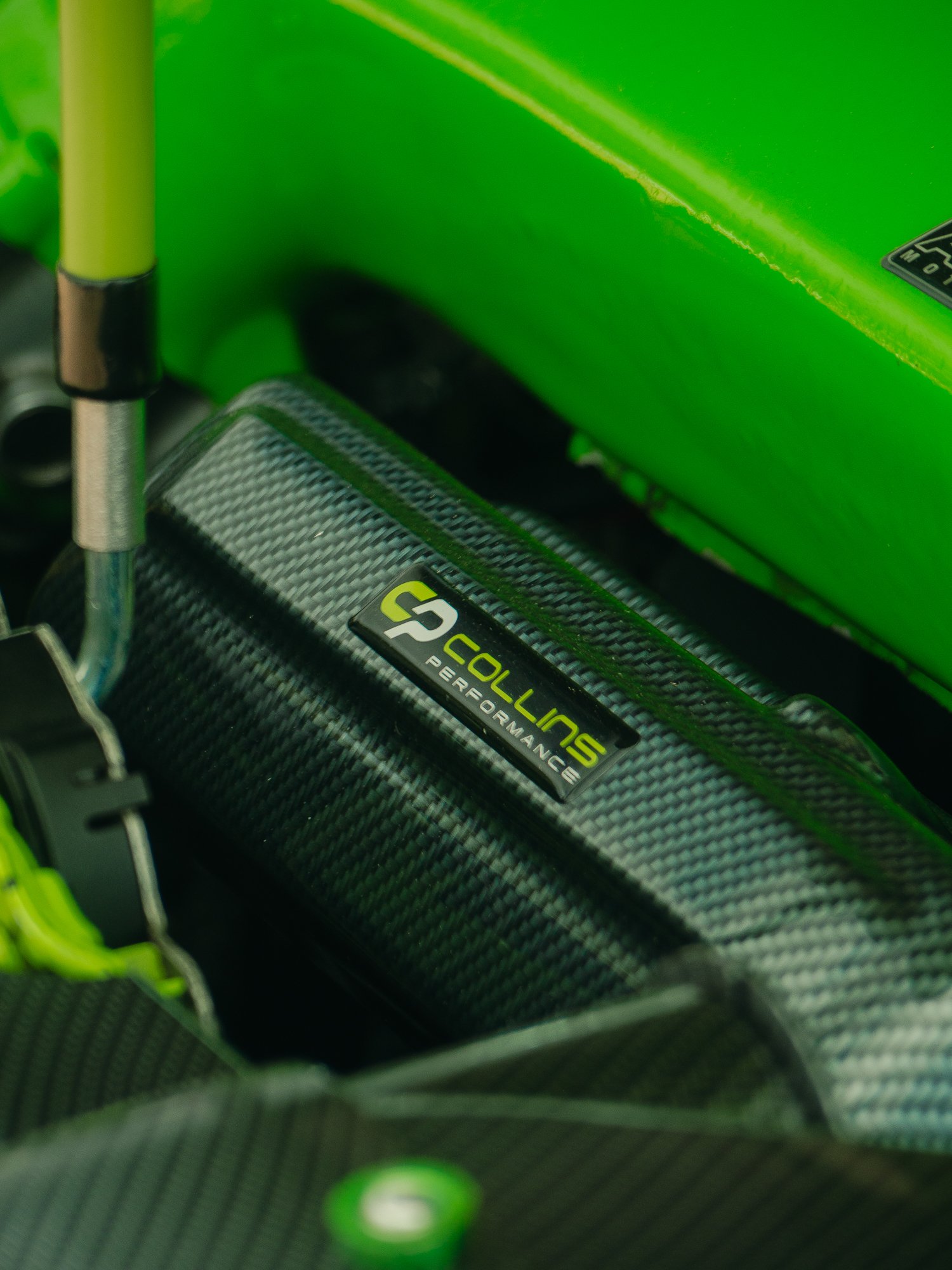 Close-up of a carbon fiber racing bike seat post with a MagnaFlow carbon fiber sticker, part of a green frame, and a black and green pedal in the background.