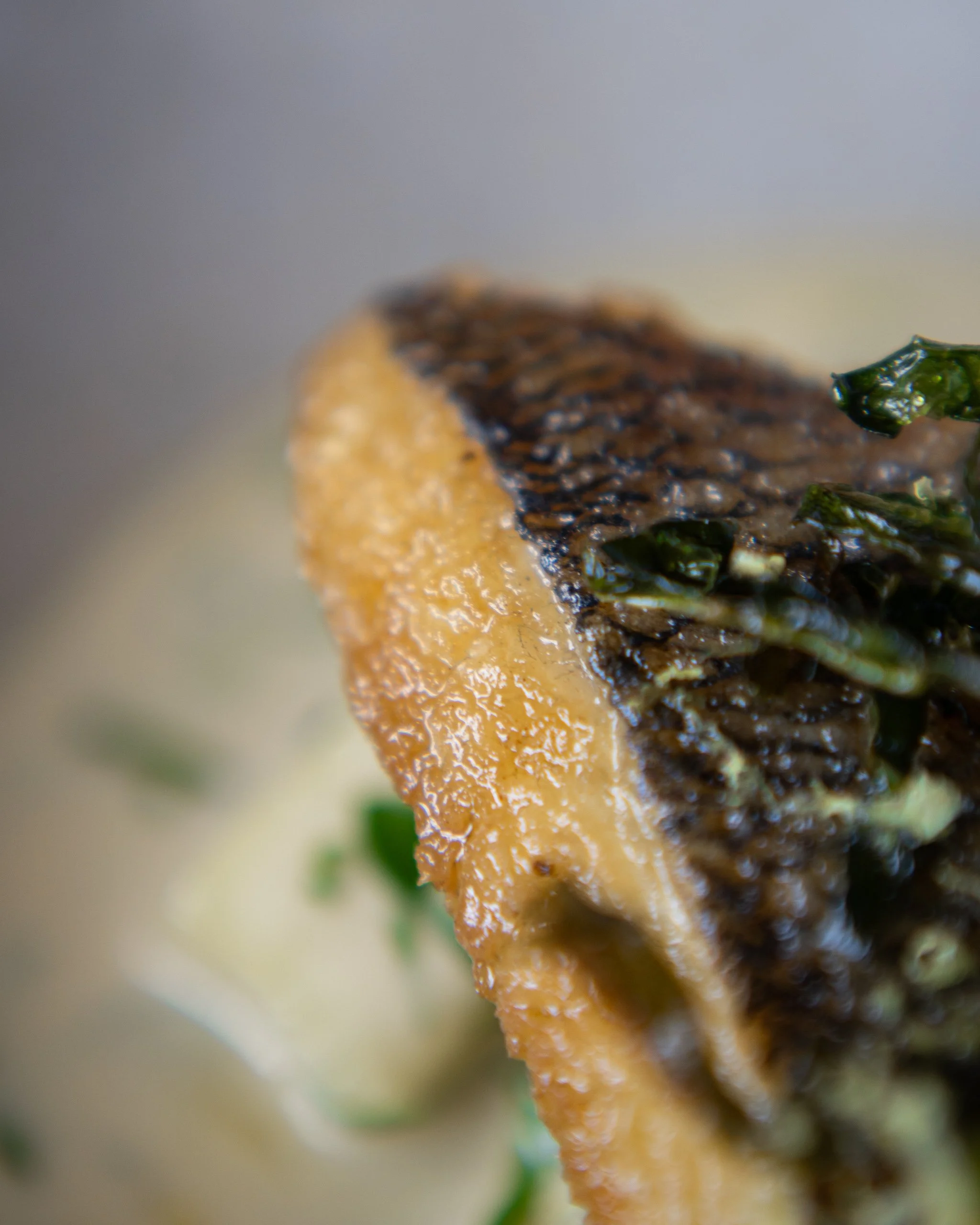 Close-up of a grilled fish fillet with crispy skin, partially covered in green garnish.