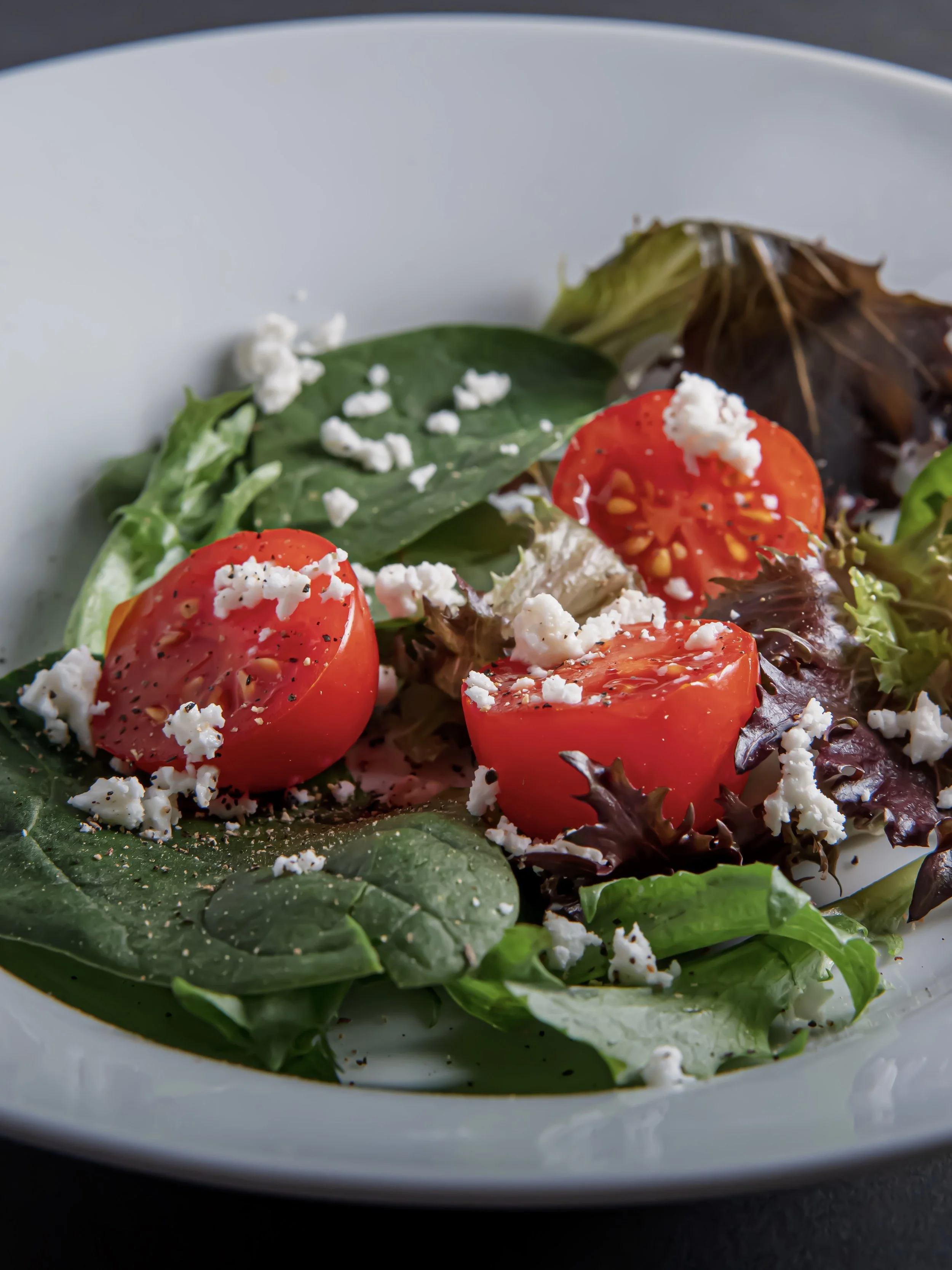 Fresh garden salad with tomatoes, leafy greens, and crumbled cheese on a white plate.