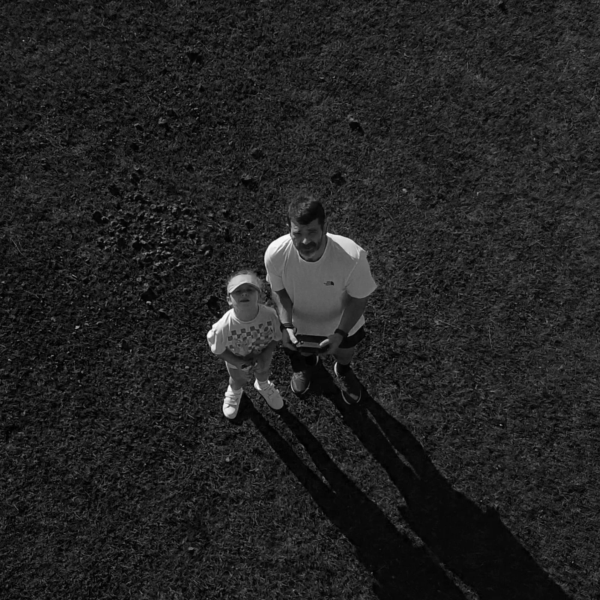 A child and an adult looking up at the camera in an outdoor grassy area.