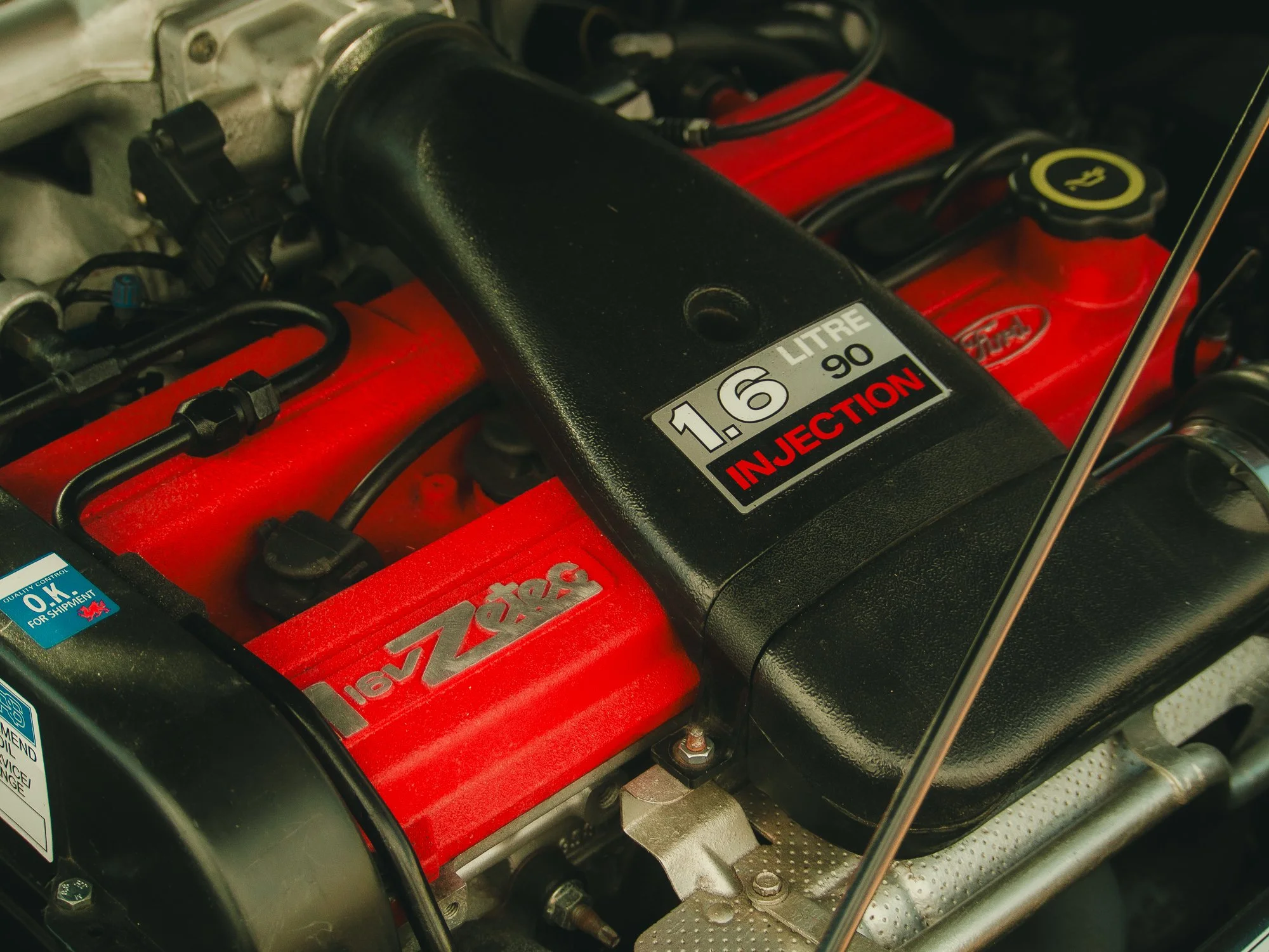 Close-up of a car engine showing a black intake manifold, red valve cover with a Lucar sticker, and various hoses and wires.