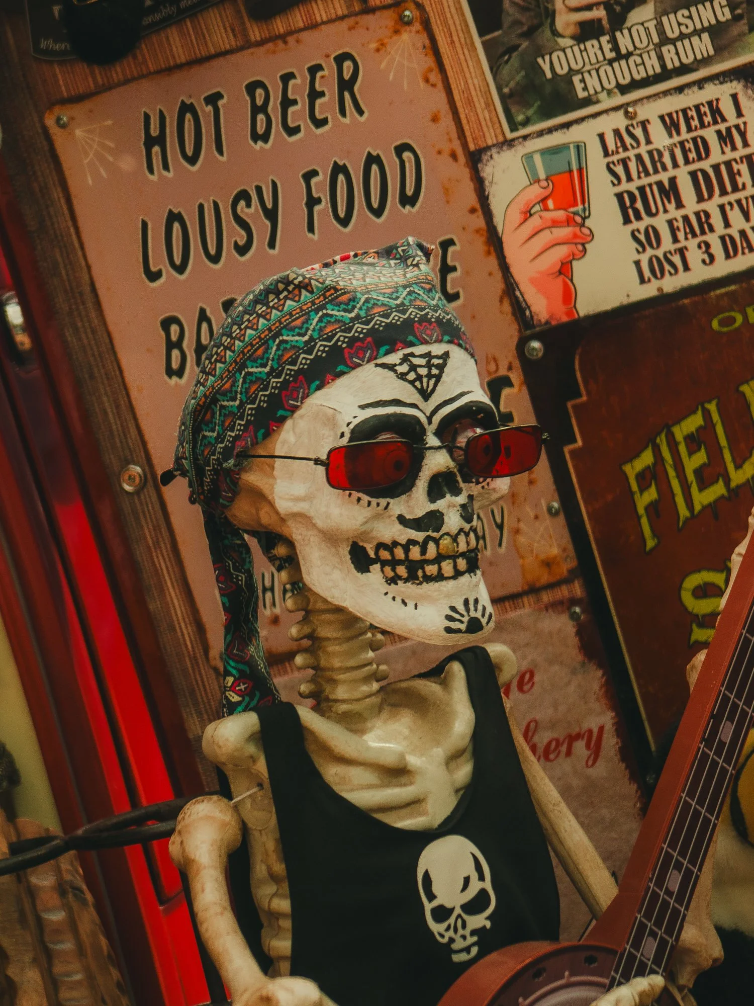 A skeleton wearing a colorful bandana and sunglasses, holding a guitar, with signs about beer and rum in the background.