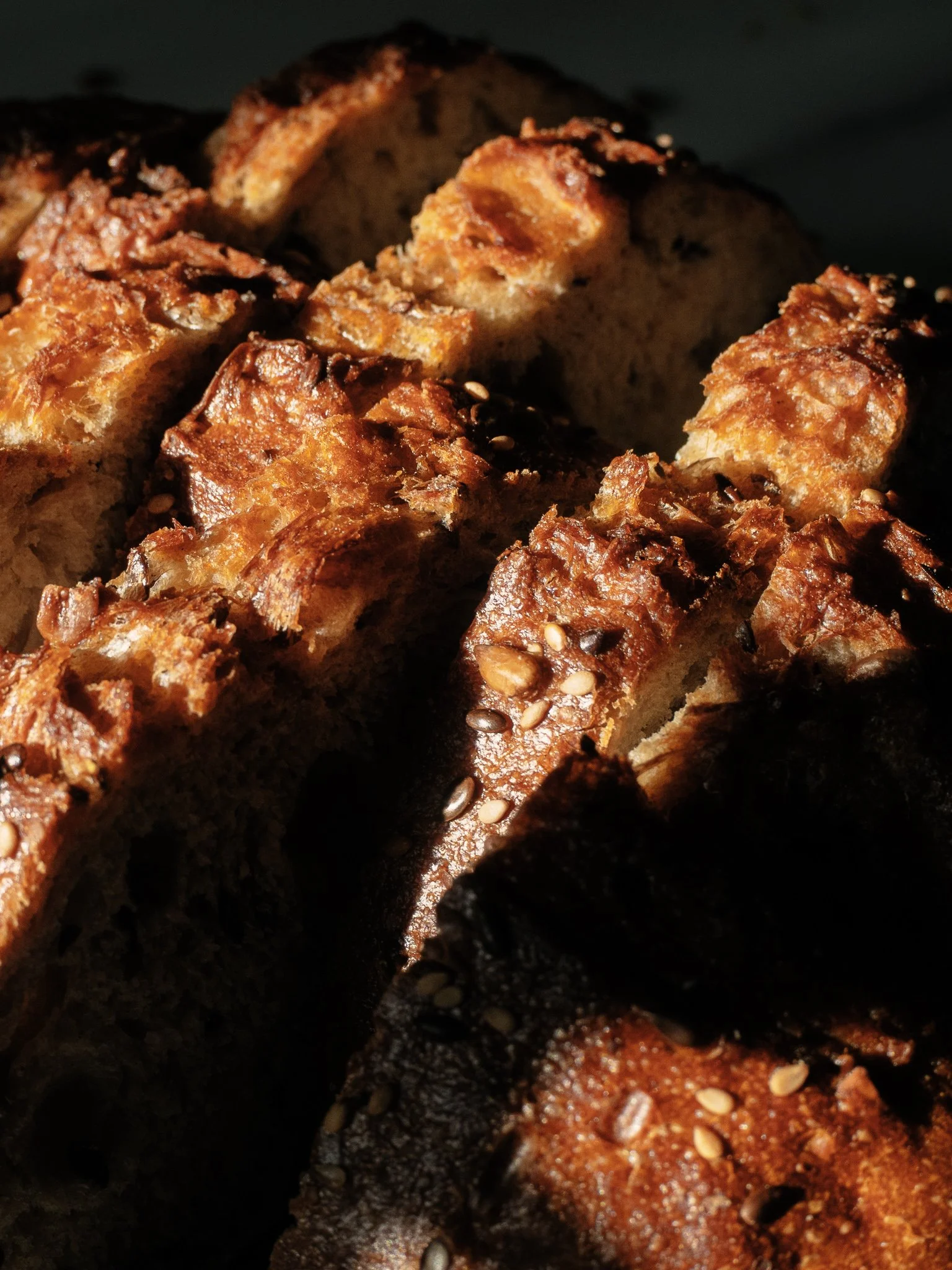 Close-up of toasted bread slices topped with sesame seeds and caramelized sugar, with dark shadows and warm light.