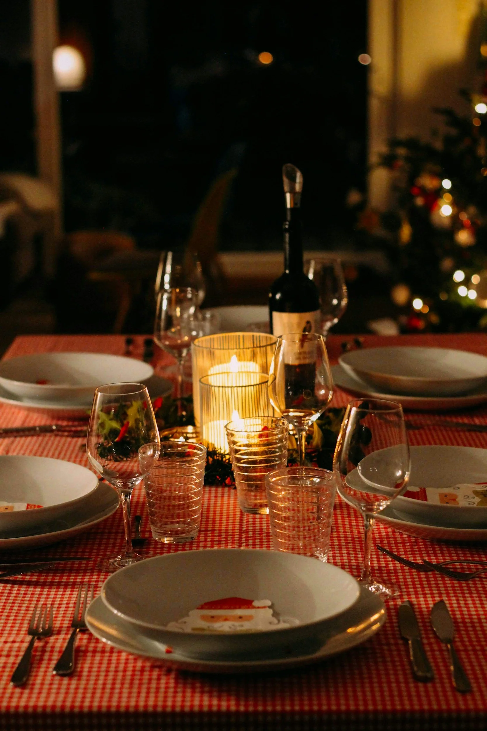 Table de dîner de Noël avec assiettes, verres, bougies, bougie et bouteille de vin, décorée avec des éléments de Noël.
