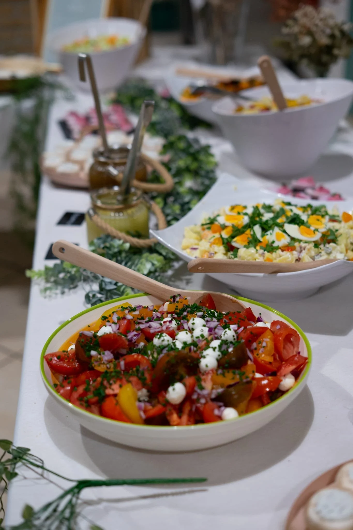 Salades colorées avec tomates, mozzarella, œufs et herbes, sur une table de buffet.
