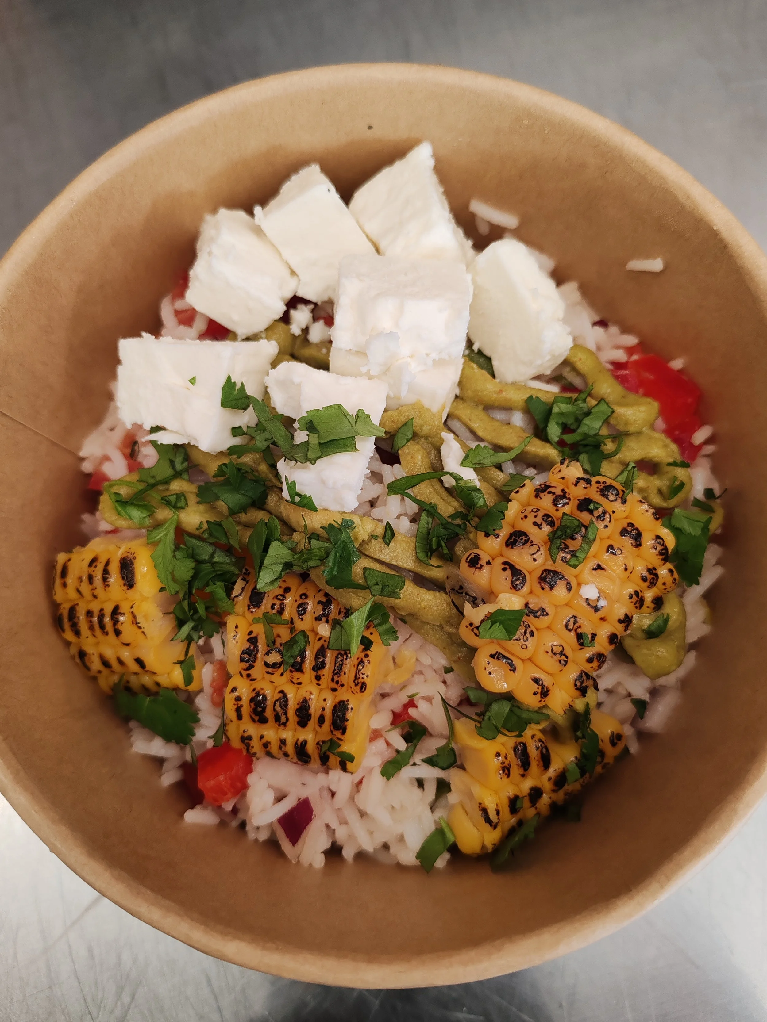 Bol de riz garni de maïs grillé, cubes de fromage, légumes verts et herbes fraîches.