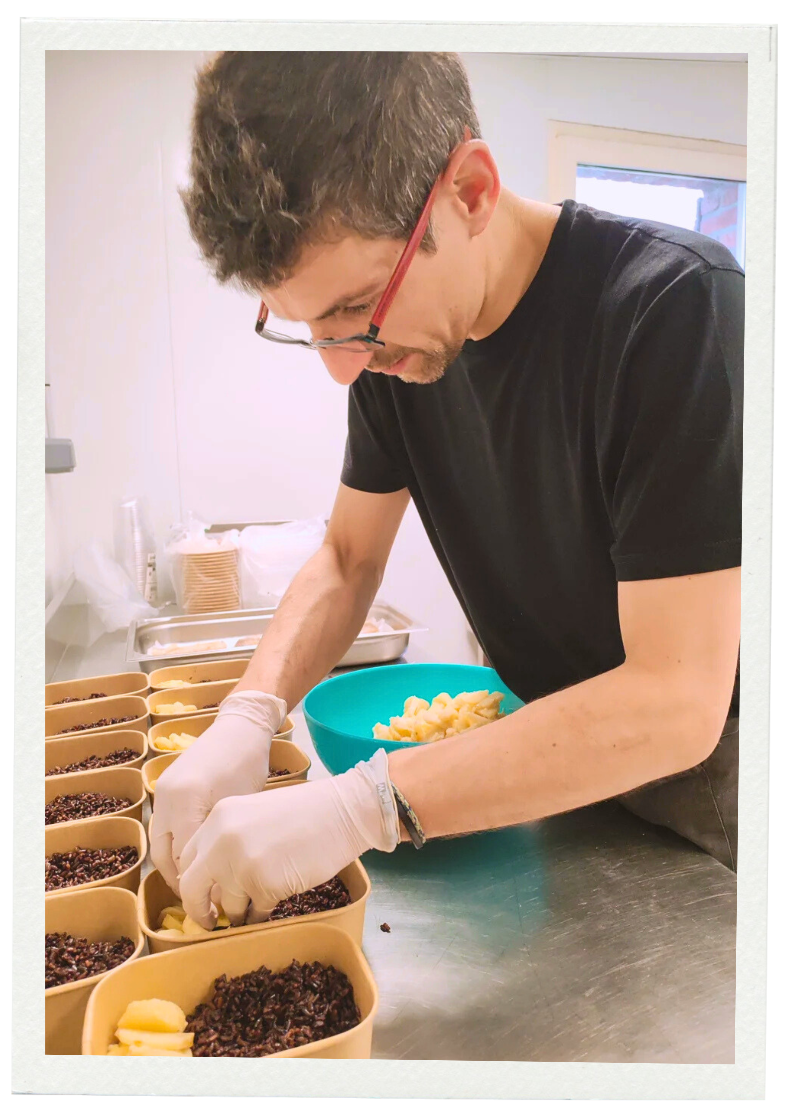 Gregory en train de préparer des plats avec du riz noir, portant des gants, dans une cuisine.