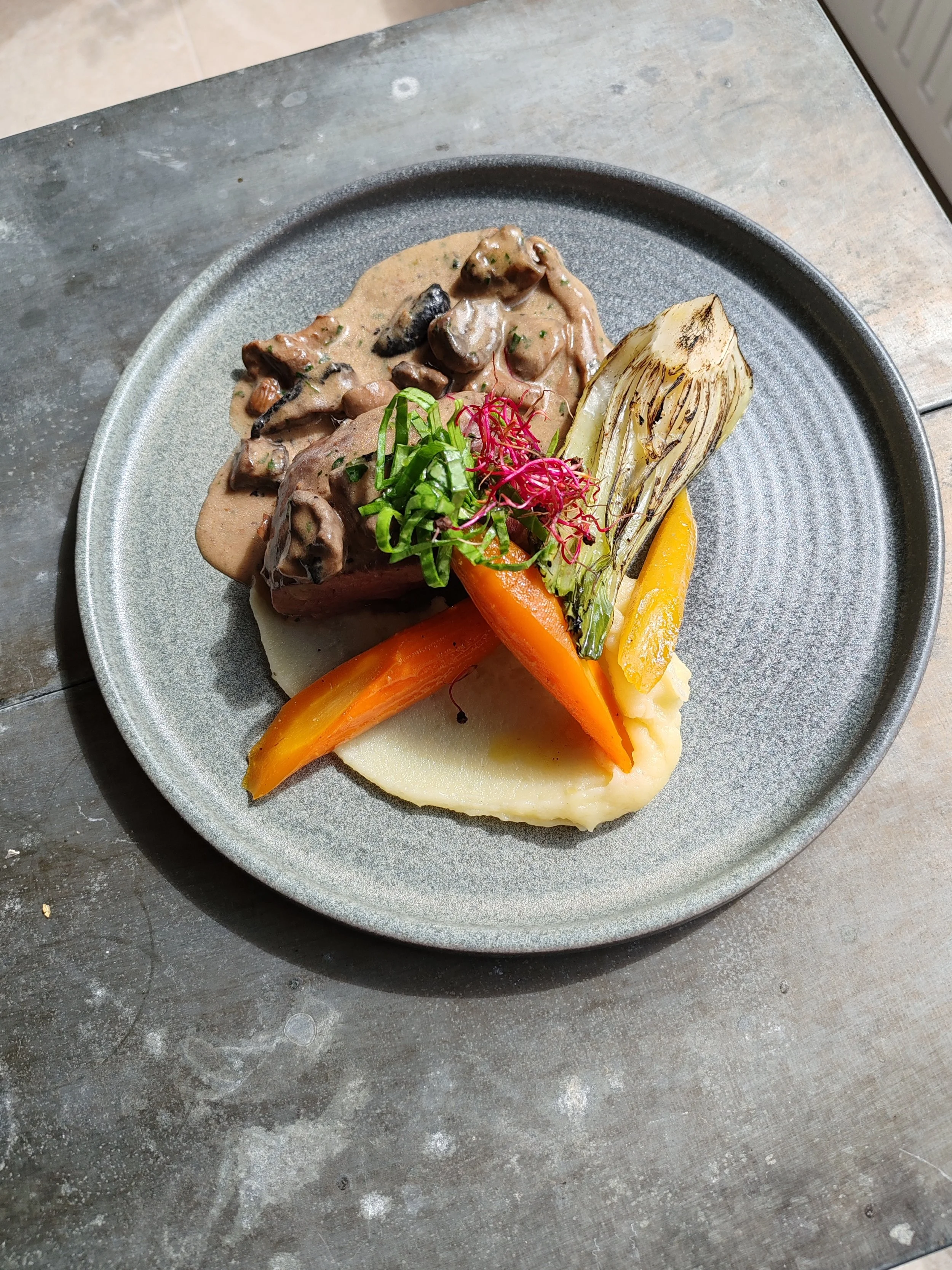 Assiette de plat avec morcillas, légumes grillés, purée, et garnitures végétales.