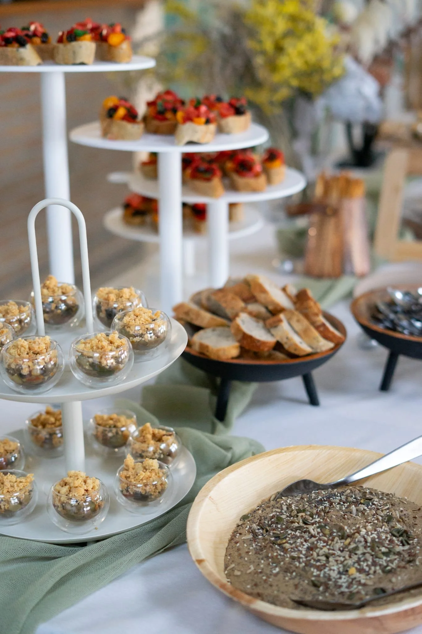 Une table de buffet avec divers desserts et plats. On voit des petits gâteaux avec des fruits rouges, des tartines de pain, des coupelles avec un crumble, et une soupe ou mousse aux graines, décorée de graines variées.