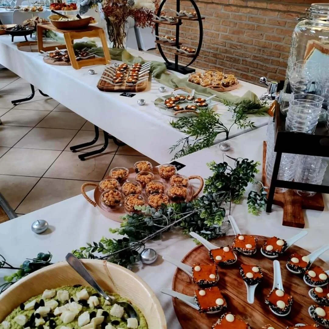 Buffet de desserts variés sur une table, avec cookies, muffins, brownies et autres pâtisseries, décorée de feuillage vert et de petites boules argentées, dans une ambiance chaleureuse.