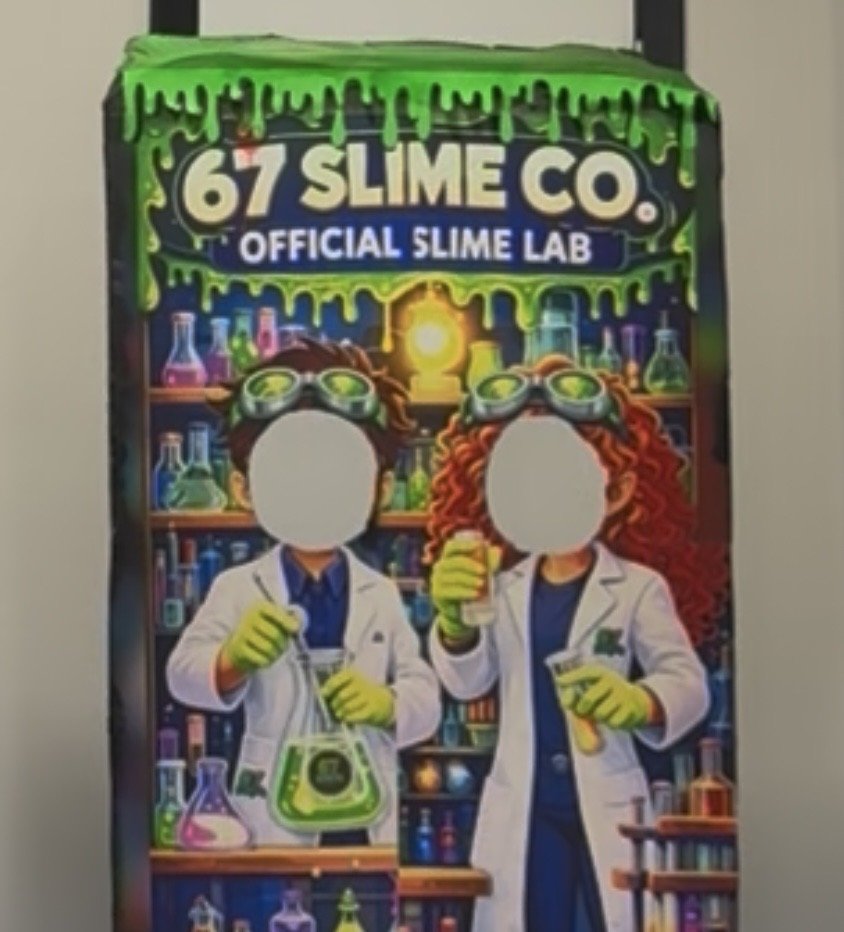 Children in science lab costumes with lab coats, gloves, and goggles, holding test tubes and beakers surrounded by shelves of colorful laboratory glassware, with green slime dripping from the top.
