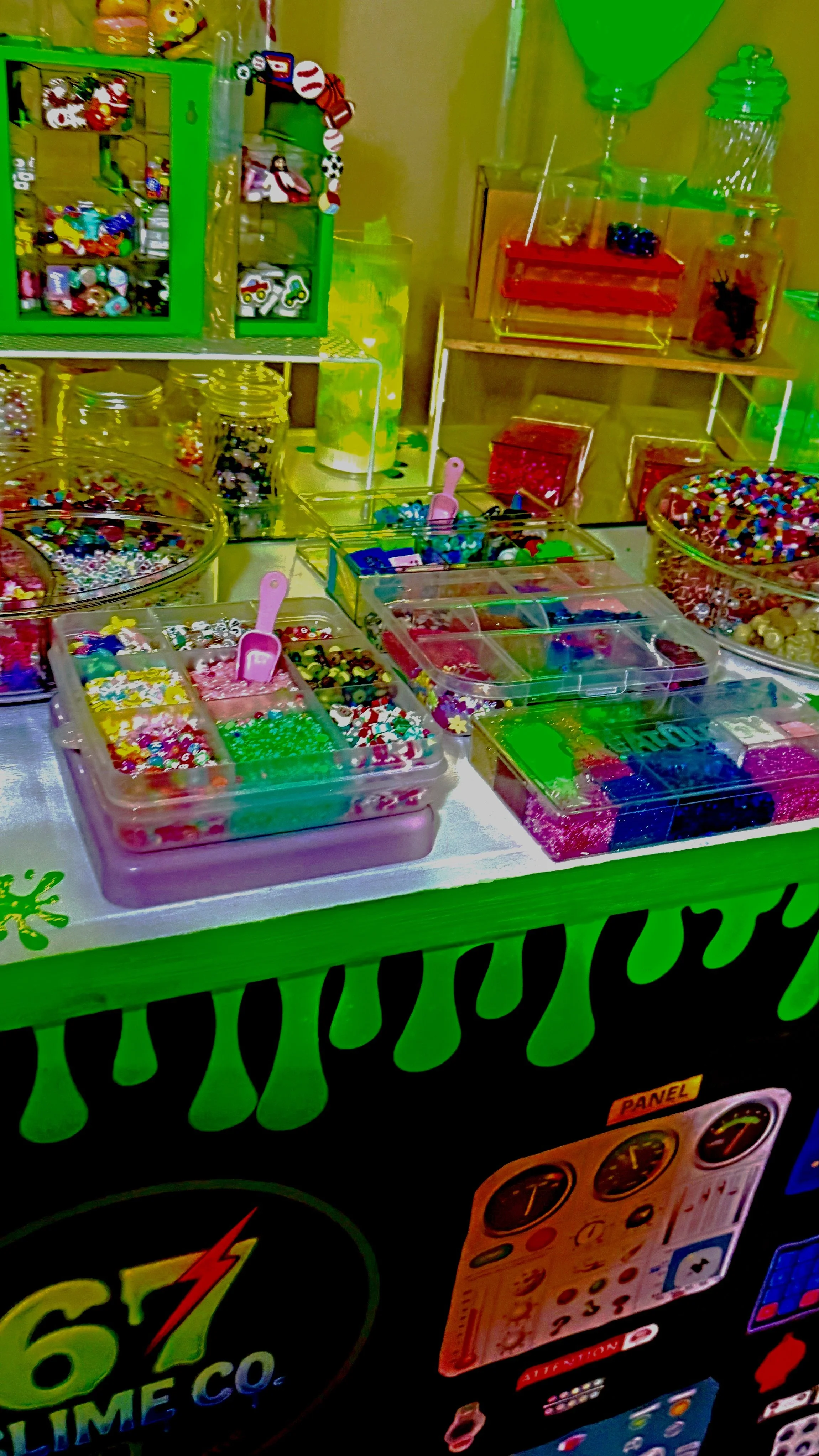 Candy and bead store display with various containers of colorful candies and beads, green and transparent display cases, and decorations in bright colors.