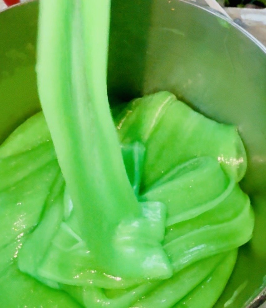 Close-up of bright green slime being poured into a container, with shiny, wet textures.