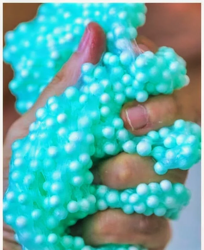 Close-up of fingers squeezing a blue slime toy with white foam beads.