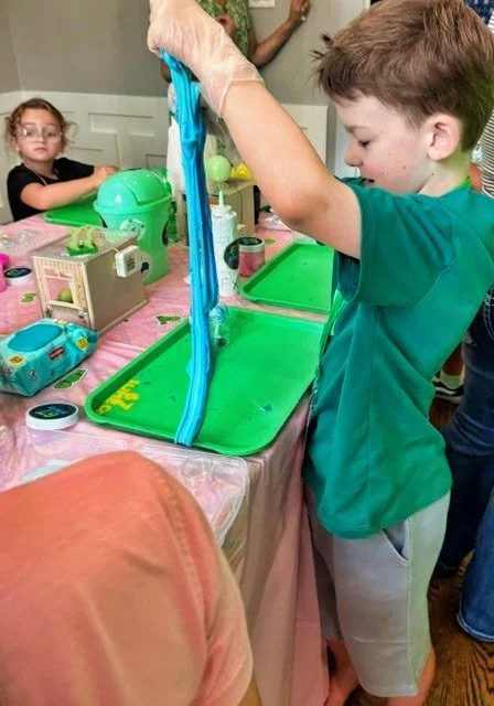 A young boy stretching his customized 67 SLIME Co. blue slime over a green tray.