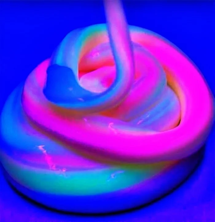 Close-up of rainbow-colored, glowing slime in a circular shape with a twisted top, illuminated under blacklight.