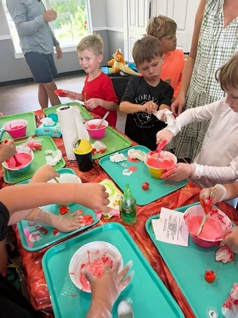 Children making homemade slime at a party, with various bowls, tools, and ingredients on the table.
