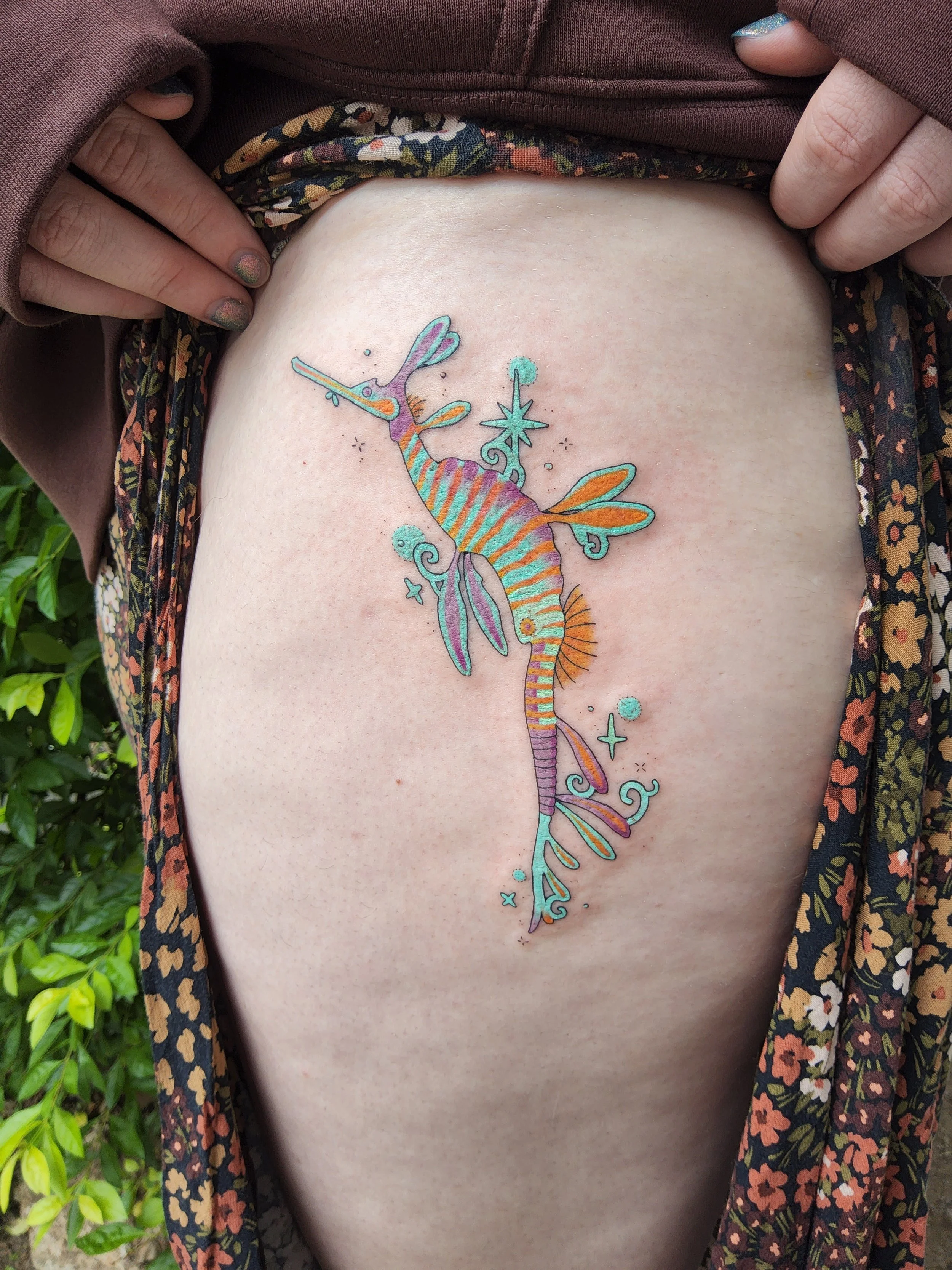 Colorful tattoo of a seahorse with whimsical details on a person's thigh.