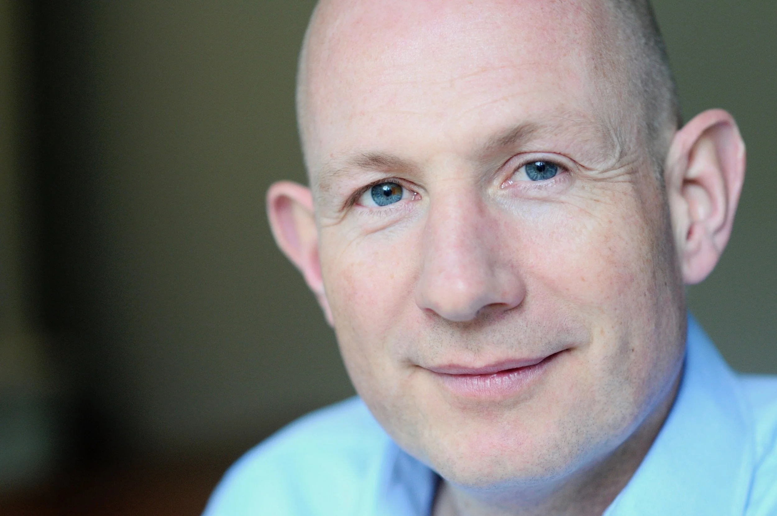 Close-up of a man with blue eyes and a friendly smile, wearing a blue shirt.