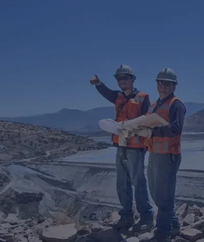 Two construction workers in helmets and safety vests reviewing plans on site, using InSAR insights to guide geotechnical risk mitigation in the field.