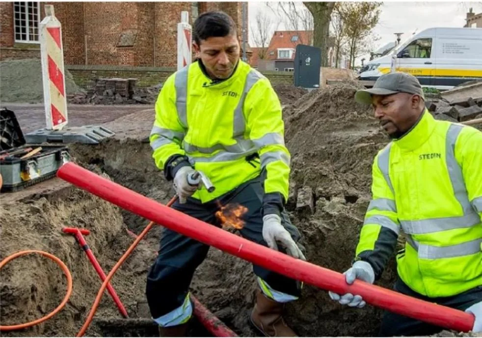 Two construction workers in high-visibility jackets working in an excavation, supported by InSAR monitoring of ground movement around buried infrastructure.