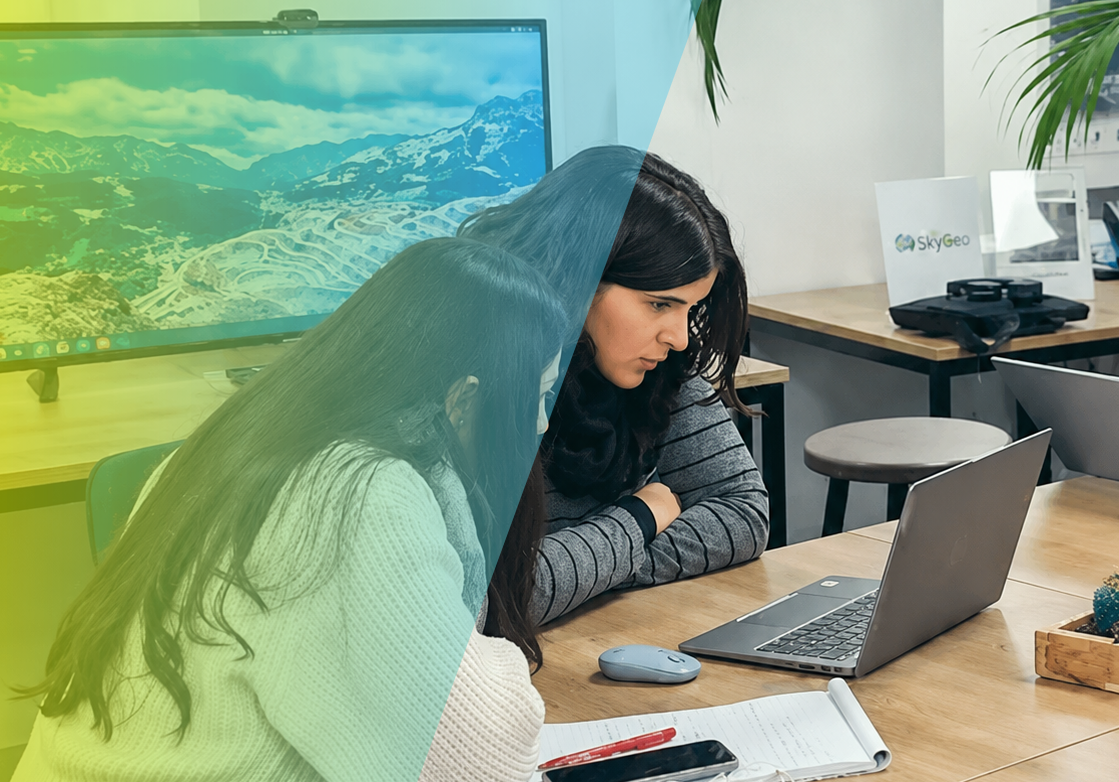 Two colleagues reviewing InSAR ground deformation results on a laptop in an office, discussing risk insights with a large landscape map on the screen.