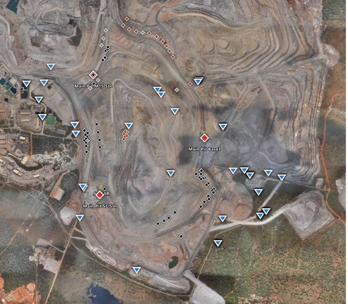 A satellite view of a large open-pit mining site with various marked points of interest, including main pits, stations, and drill sites, surrounded by roads and vegetation.