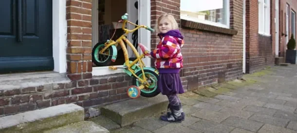 Young girl with a bicycle outside a brick house, representing how InSAR-driven ground stability monitoring helps protect everyday homes and communities.