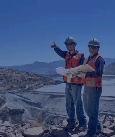 Two construction workers in helmets and safety vests reviewing plans on site, using InSAR insights to guide geotechnical risk mitigation in the field.