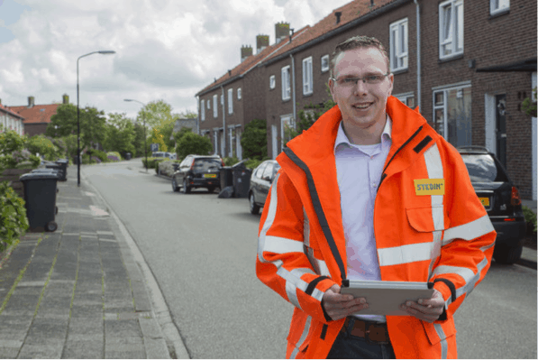 Field engineer in an orange safety jacket using a tablet to review SkyGeo InSAR ground deformation data for a residential street.