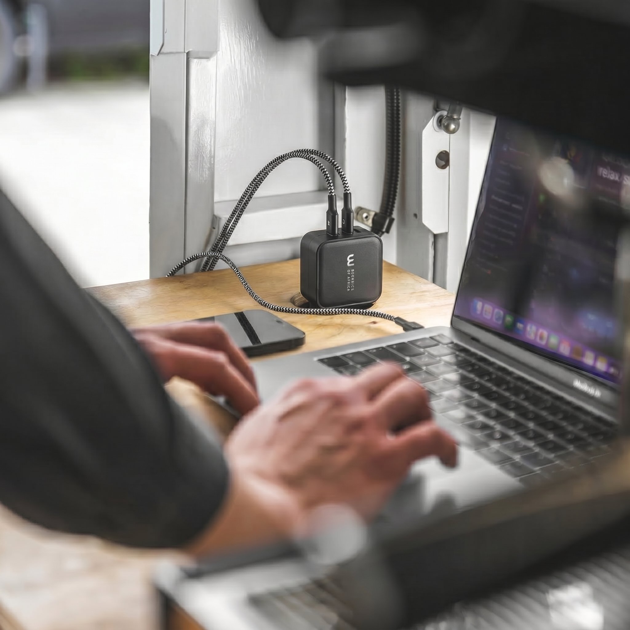 Une personne utilisant un ordinateur portable, avec un chargeur wicaya reliée à une prise électrique sur un bureau en bois, dans un environnement de bureau.