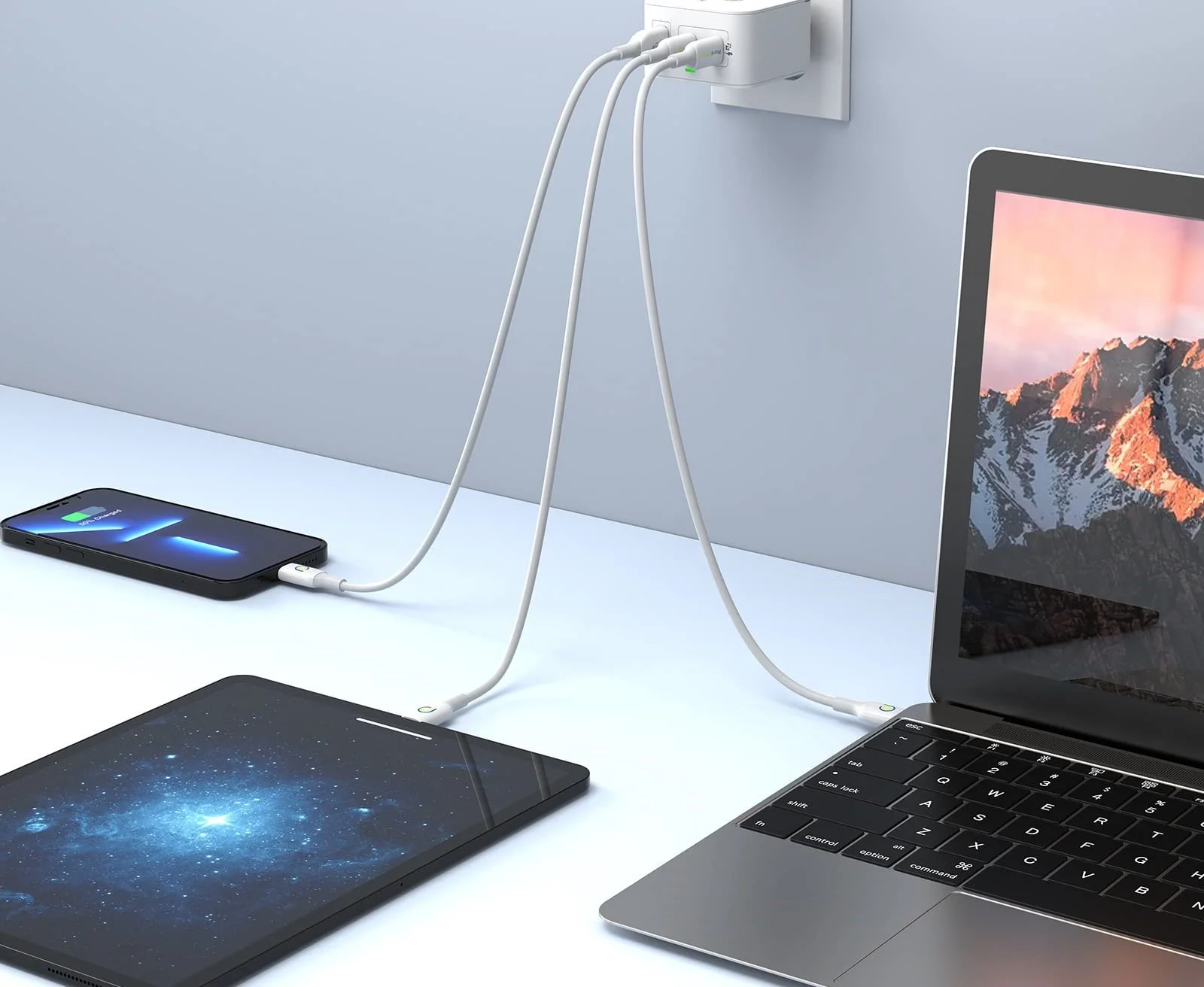 Un ordinateur portable et une tablette sont connectés à une source électrique par des câbles, avec un smartphone connecté à la tablette pour la charge, sur un bureau blanc.