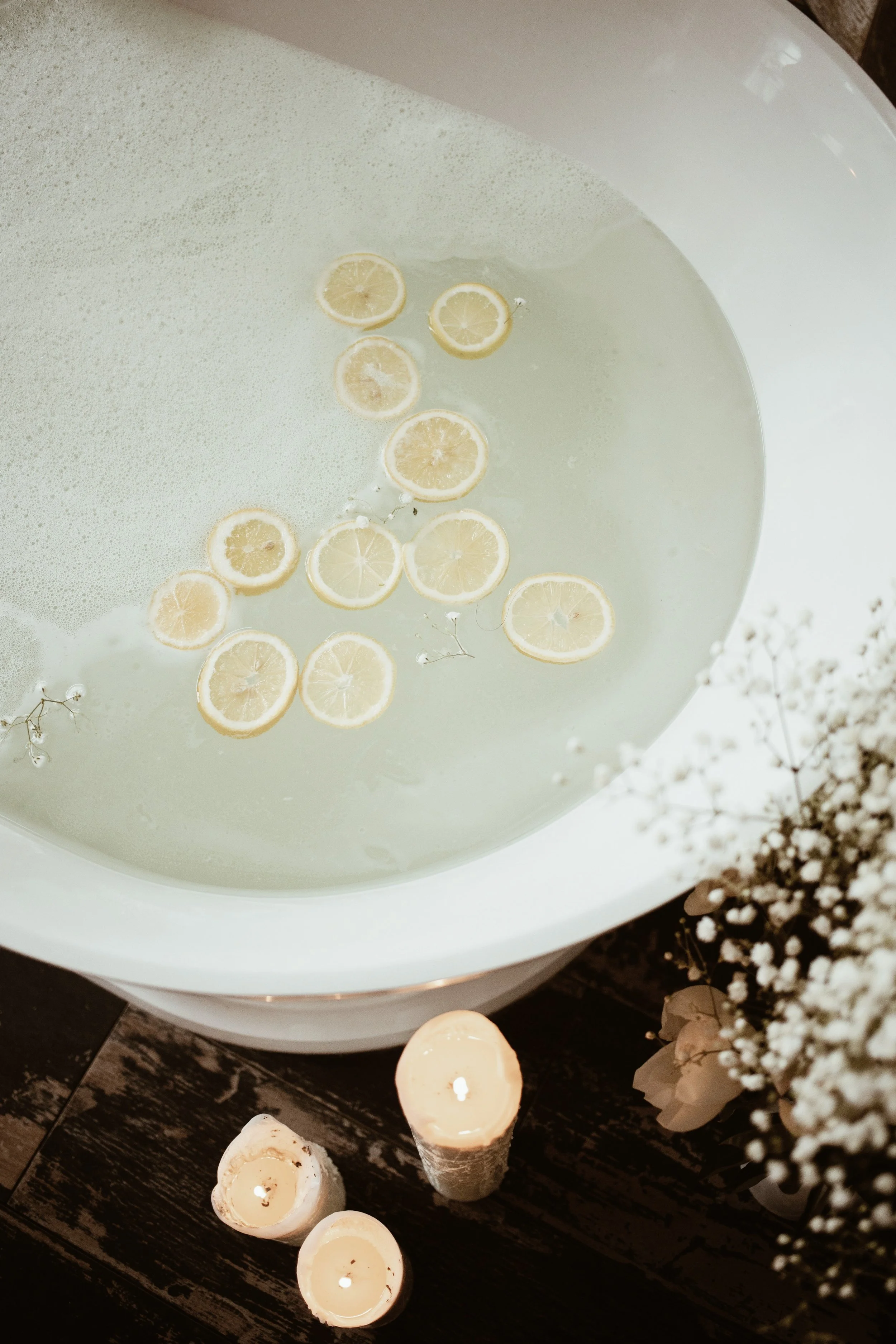 A sink filled with water and lemon slices floating on top, with candles and flowers nearby.