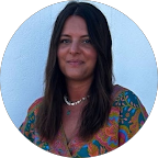 Portrait d'une femme avec des cheveux longs noirs, portant un collier et un vêtement coloré, sur fond bleu