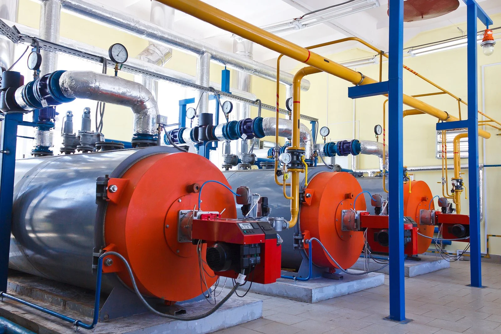 Industrial boiler system with large pressure gauges, insulated pipes, and control panels in a bright, clean room.