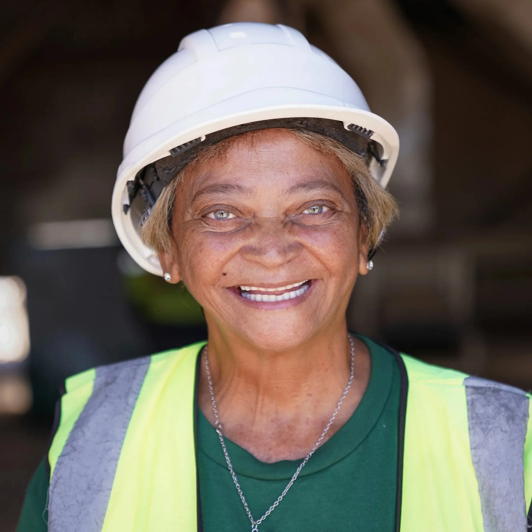 Close-up of smiling woman wearing a construction hard hat and safety vest.