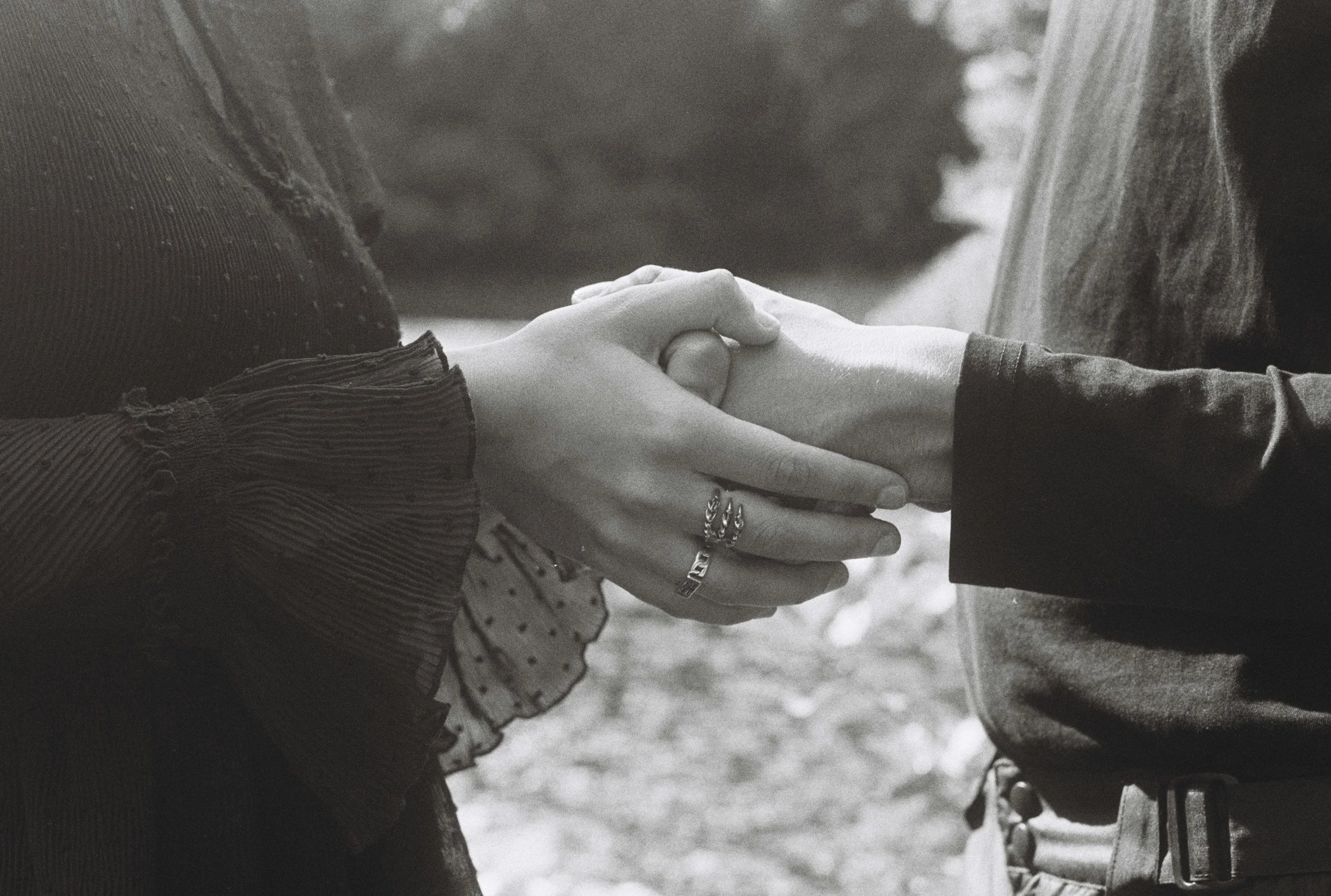 Nahaufnahme von zwei Personen Hand in Hand, die sich liebevoll halten, im Freien, in Schwarz-Weiß