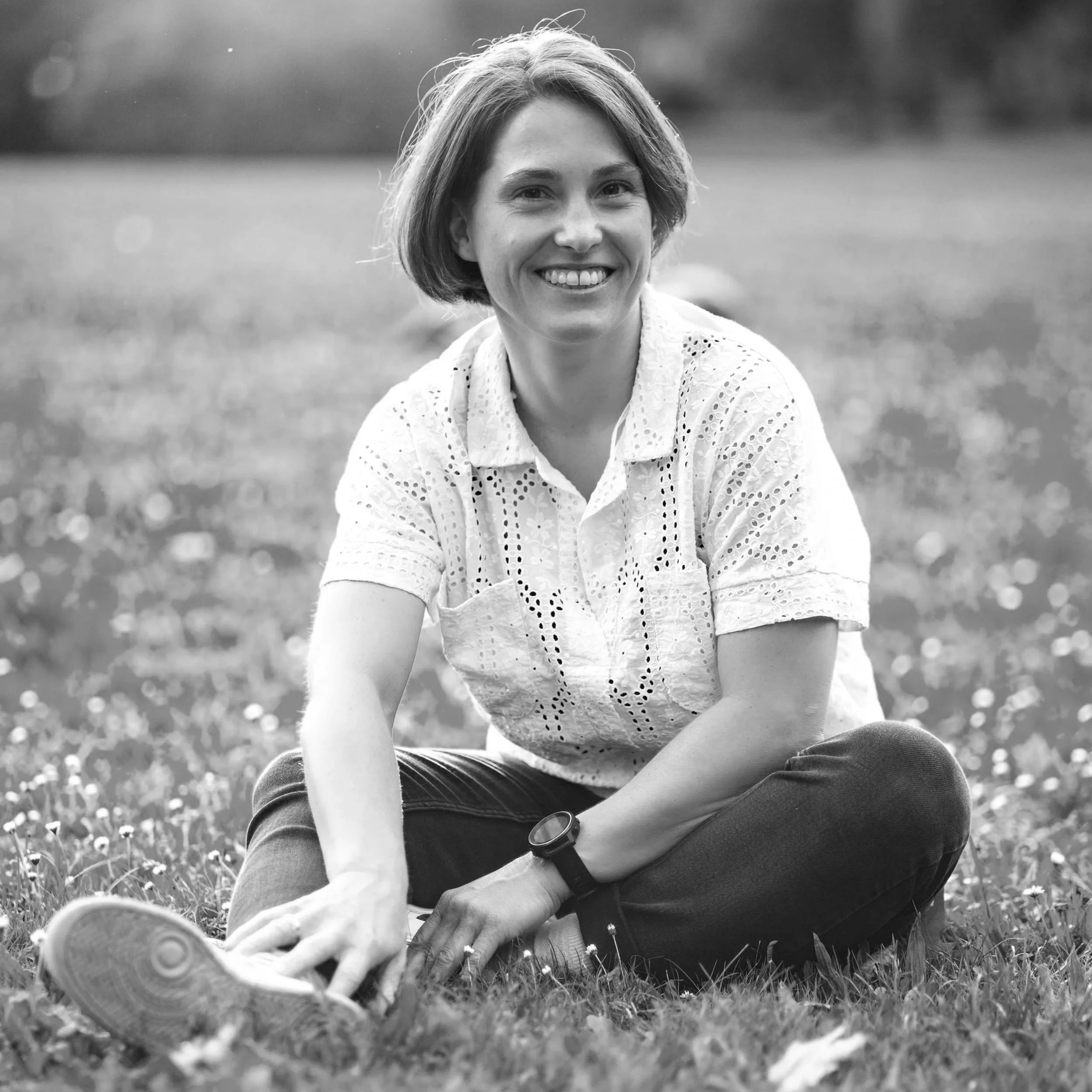 Frau sitzt lachend im Gras in einem Park, in Schwarz-Weiß-Fotografie.