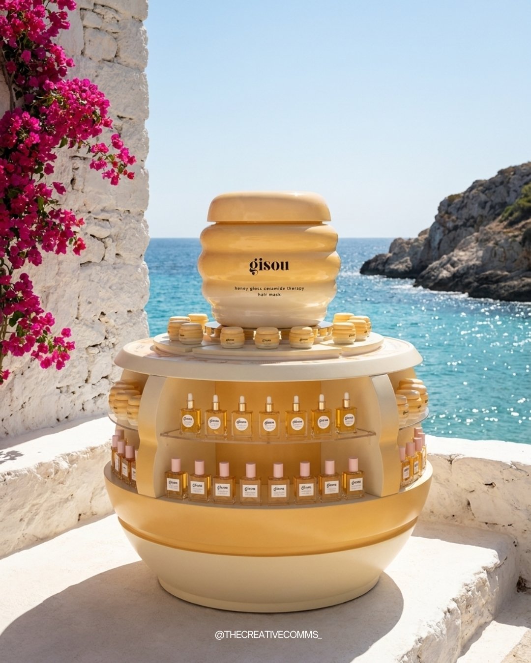 Stand de productos de belleza y cuidado de la piel junto al mar, con fondo de cielo azul y rocas, decorado con flores rosadas.