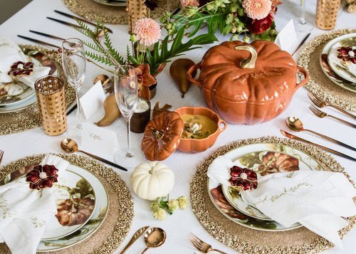 Fall-themed table setting with pumpkin-shaped decorations, floral centerpieces, and elegant plates and glassware for a festive meal.