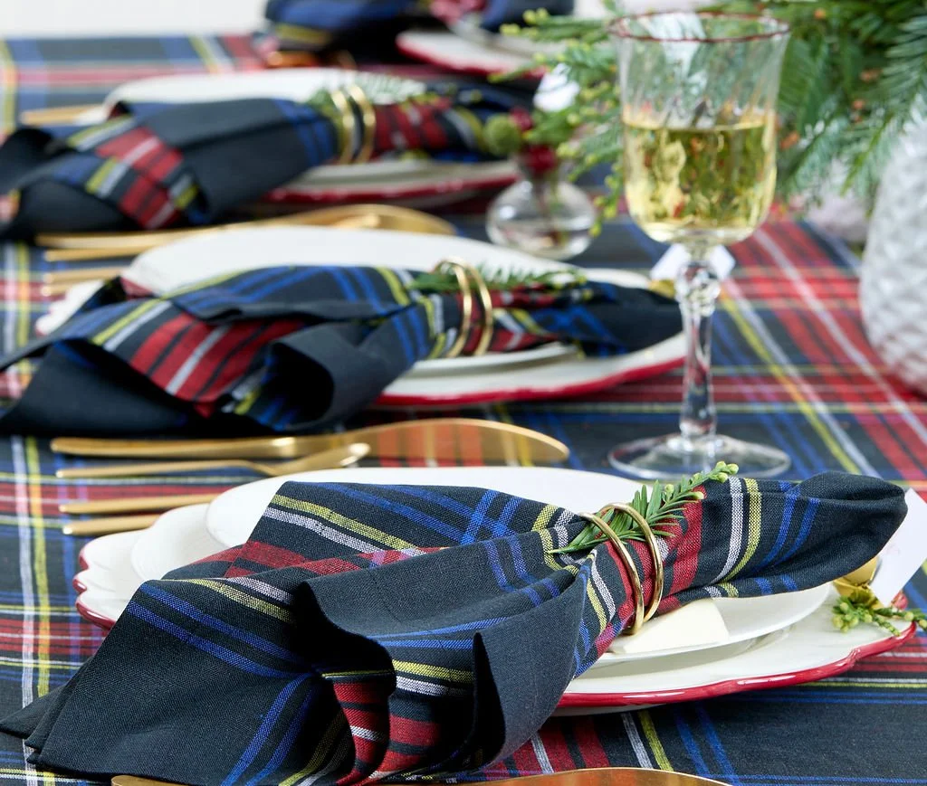 A festive table setting with plaid napkins, gold flatware, and a wine glass containing a floral arrangement, decorated for a celebration or holiday.