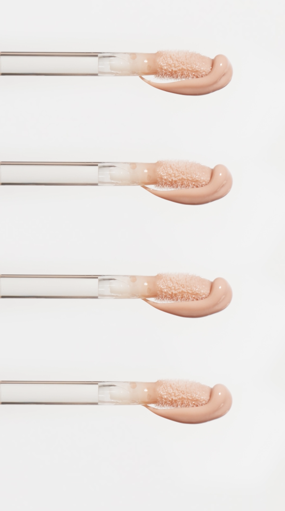 Four lip gloss applicators with peach-colored gloss on white background.