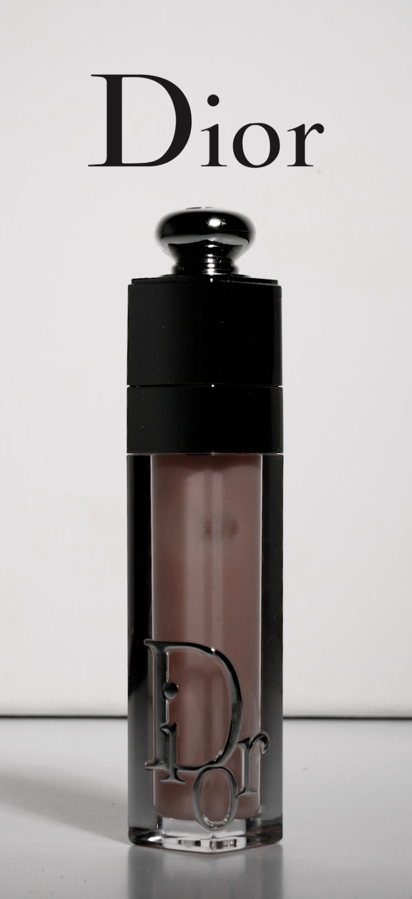 A Dior lipstick with a black cap and clear body, displaying a pinkish tone lipstick inside, placed in front of a white background with the Dior logo at the top.