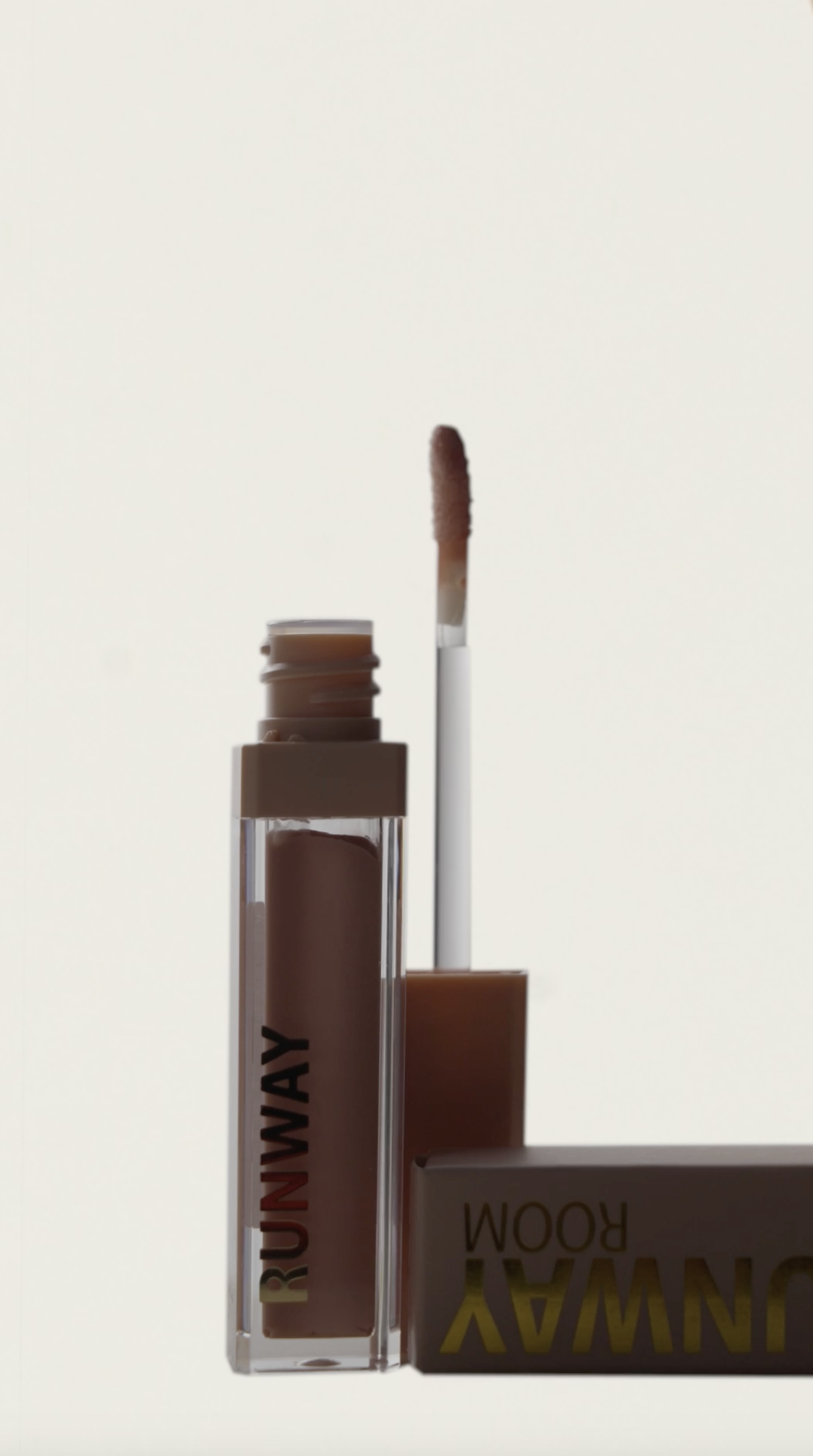 Close-up of a nude-colored lip gloss or lipstick tube with the cap removed, showing the applicator wand with product, against a plain background.