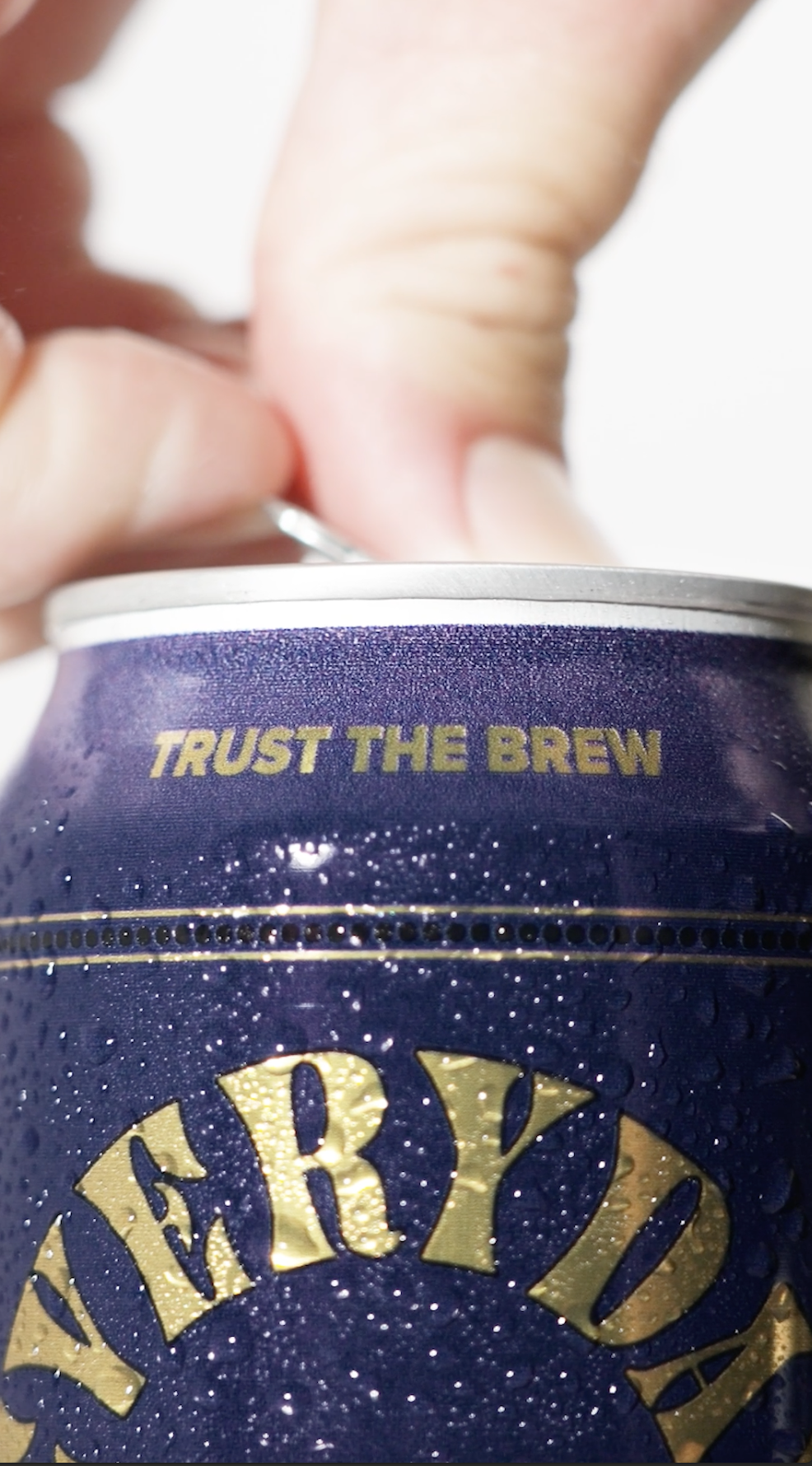 Close-up of a soda can with the words "Trust the Brew" and part of the brand name "Feryd" visible, wet with condensation, with a person's fingers in the background.