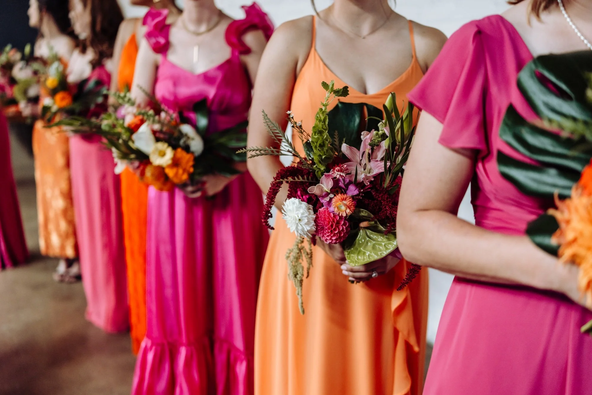 Women in colorful dresses holding bouquets of flowers, standing in a line, during a wedding.